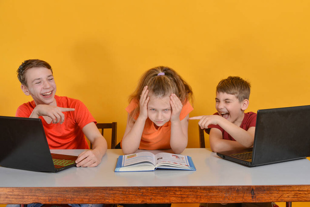 Kinderen worden thuis opgeleid, twee jongens zitten achter een laptop, een meisje leest boeken. Online leren thuis concept. - Foto, afbeelding