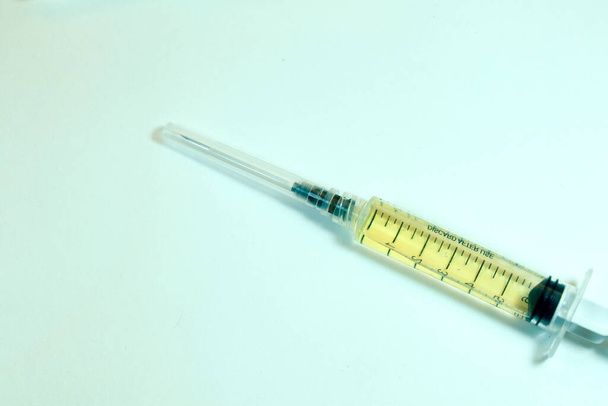 Medische naald op de steriele tafel met vloeibaar vaccin, geel vaccin tegen virussen. Vaccinatie en antibiotica. Studiosessie. - Foto, afbeelding