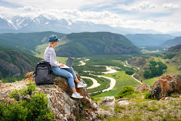 A woman working on a laptop on the top of the mountain. Freelancer relaxing in mountains. Remote work, outdoor activity in summer. - Foto, Imagem