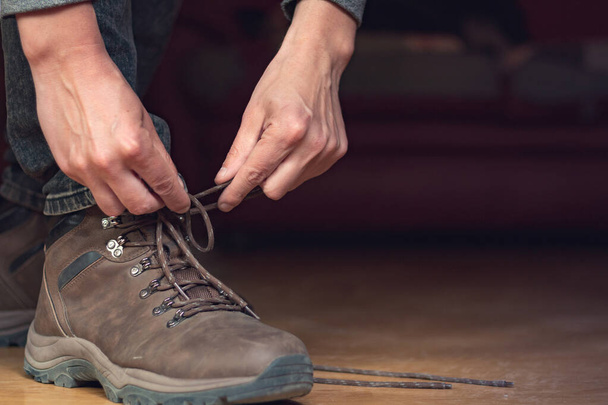 El hombre se pone sus botas de cuero en la frente, ata el cordón largo del zapato
 - Foto, Imagen