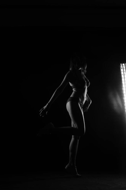 σιλουέτα της όμορφης γυναίκας με σύντομη ακούσει σε εσώρουχα ποζάρουν σε σκούρο φόντο στούντιο     - Φωτογραφία, εικόνα