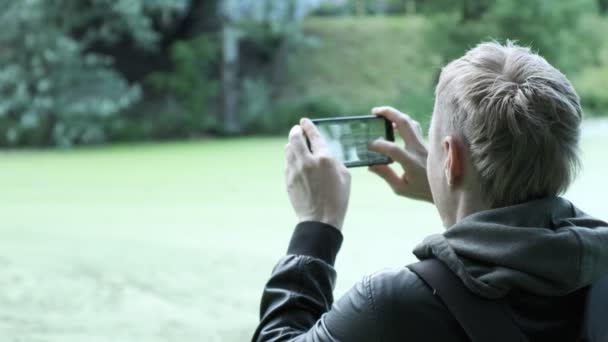 mies ottaa kuvia ankoista älypuhelimella. luonnonvaraisten eläinten ottaminen kuvia linnuista - Materiaali, video