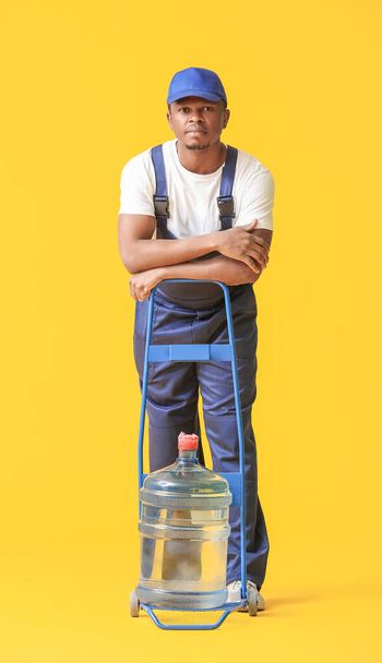 African-American delivery man with bottle of water on color background - Foto, afbeelding