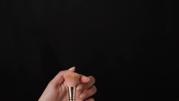 Woman with makeup brush sprinkling cosmetic powder on dark background - Filmagem, Vídeo