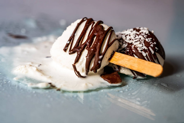 Nanuková zmrzlina s čokoládovou polevou posypaná strouhaným kokosem na oroseném skleněném pozadí se rozpouští, detailní záběr. - Fotografie, Obrázek