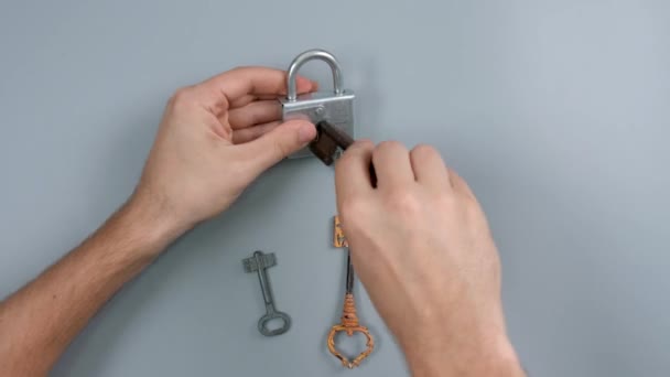 L'homme qui choisit la clé pour ouvrir le cadenas sur fond gris, vue de dessus - Séquence, vidéo