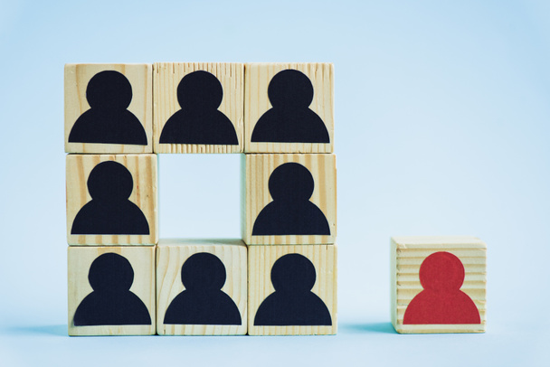 vierkant van houten blokken met zwarte menselijke iconen en rood stuk op blauwe achtergrond, leiderschap concept  - Foto, afbeelding