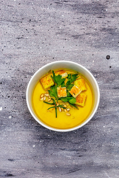Żółta zupa z cukinii. Zdrowe wegańskie (wegetariańskie) jedzenie, chrupiące tosty, nasiona słonecznika, świeże warzywa. Szary kamień beton tło, widok z góry - Zdjęcie, obraz