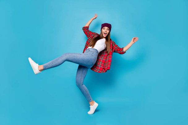Full length profile photo of good mood pretty lady warm spring weather rejoicing raise leg walking street excited wear casual hat plaid shirt jeans shoes isolated blue color background - Фото, изображение