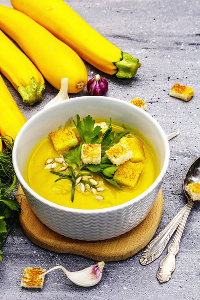 Жовтий кабачковий вершковий суп. Здорова вегетаріанська (вегетаріанська) їжа, хрусткий тост, насіння соняшнику, цілі стиглі фрукти, свіжа зелень. Сірий кам'яний бетонний фон, крупним планом
 - Фото, зображення
