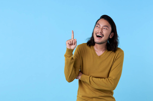 Wow e surpreendido jovem asiático homem sorrindo com o dedo apontando no fundo azul com espaço de cópia
. - Foto, Imagem
