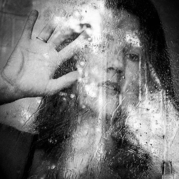 κορίτσι πίσω από το γυαλί στο οποίο σταγόνες βροχής, υγρό γυαλί μετά τη βροχή, η αντανάκλαση μιας γυναίκας - Φωτογραφία, εικόνα