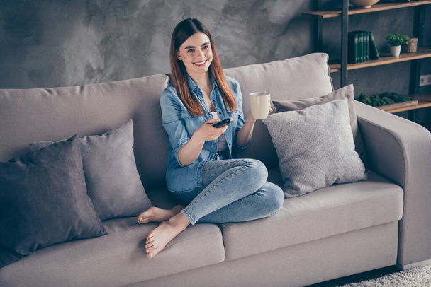 Photo of positive cheerful girl sit comfy divan watch film hold remote control switch channels in living room apartment house indoors - Photo, image