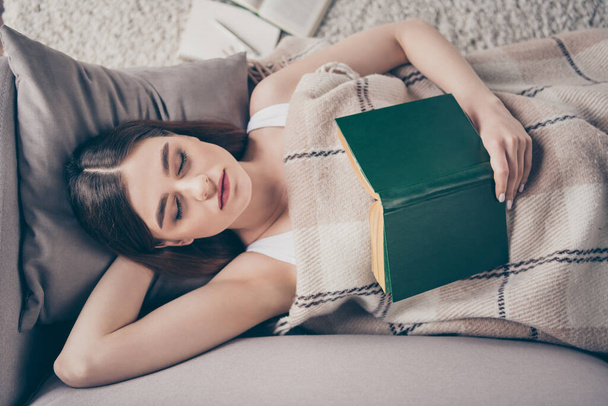 Late evening reading book concept. High angle view photo of peaceful girl hold poetry textbook sleep cover close checkered plaid blanket lie divan in apartment room indoors - Foto, imagen
