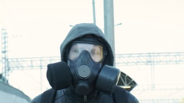 homem com máscara de gás, casaco com capuz andando ao ar livre na frente do trem em movimento
 - Filmagem, Vídeo
