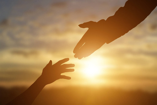 Silhouet van het geven van een helpende hand, hoop en steun elkaar over zonsondergang achtergrond. - Foto, afbeelding