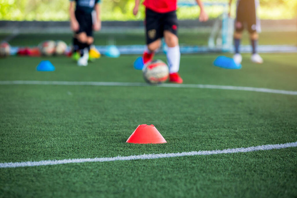Cone marker is soccer training equipment on green artificial turf with blurry kid players training background. Material for trainning class of football academy. - Фото, зображення