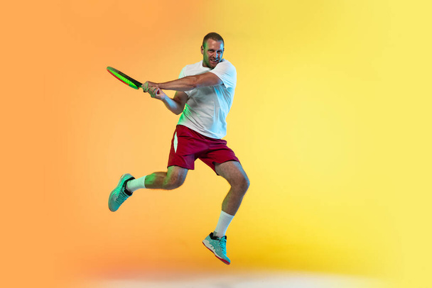 Hombre caucásico deportista profesional jugando al tenis en el fondo del estudio en luz de neón
 - Foto, Imagen