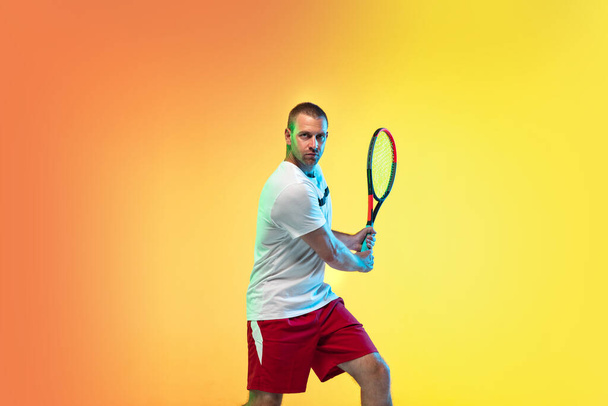 Caucasian male professional sportsman playing tennis on studio background in neon light - 写真・画像