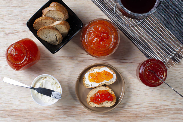 Mesa con tostadas acompañadas de cuajada y mermeladas de pimienta. Vaso de jugo de uva en el fondo
 - Foto, imagen