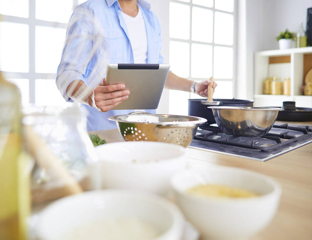 Man following recipe on digital tablet and cooking tasty and healthy food in kitchen at home - Foto, imagen