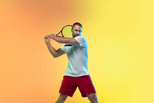 Caucasian male professional sportsman playing tennis on studio background in neon light - Foto, Imagen