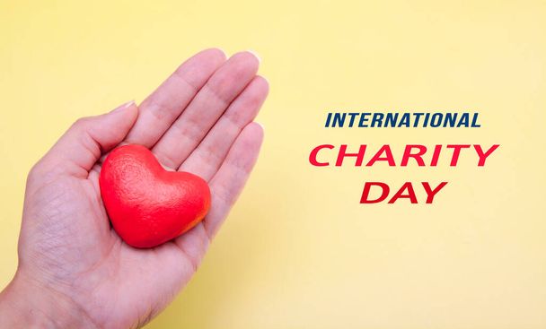 Coeur rouge à la main sur fond jaune avec texte Journée internationale de la charité - Photo, image