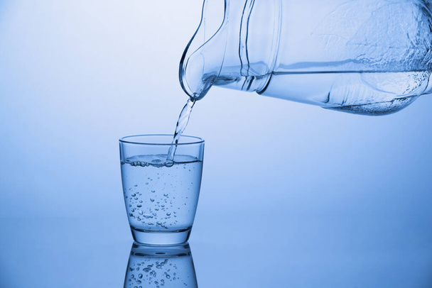 Verter agua de una jarra en un vaso sobre fondo azul
 - Foto, imagen