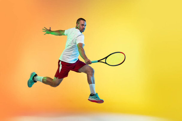 Caucasian male professional sportsman playing tennis on studio background in neon light - Fotó, kép