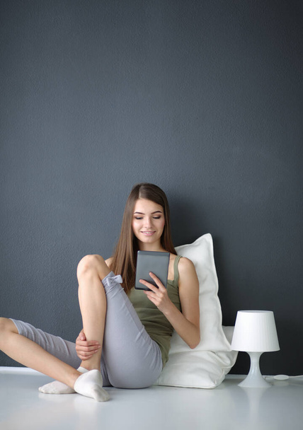 Beautiful young woman sitting on floor with tablet - Foto, afbeelding