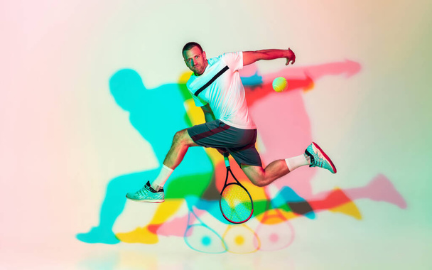 Caucasian male professional sportsman playing tennis on studio background in neon light - Photo, Image