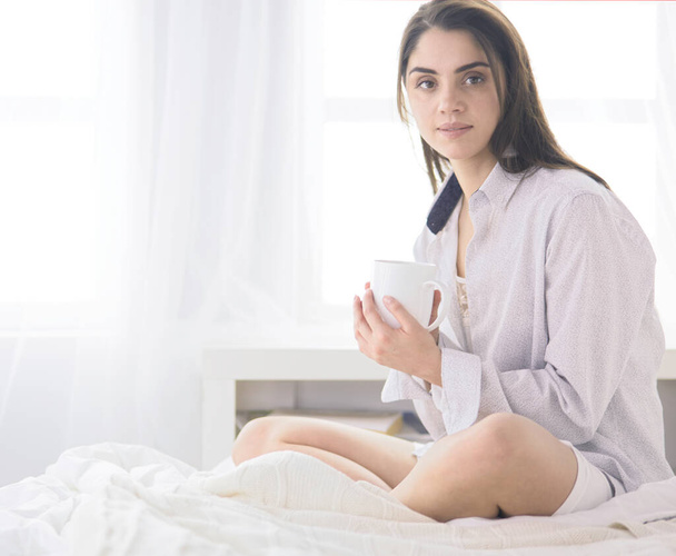 Жінка сидить у ліжку читає книгу і снідає
 - Фото, зображення