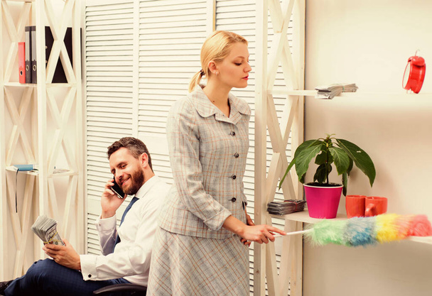 Gender concept. Gender and career. Personal assistant. Equal rights for education work and salary. Gender discrimination in business life. Woman cleaning up office while boss has phone conversation - 写真・画像