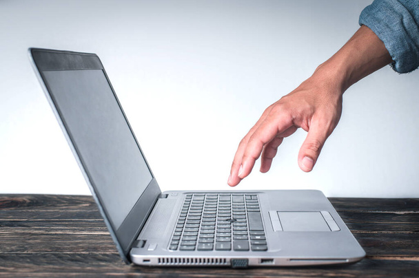 Egy férfi keze farmeringben egy gesztust mutat az asztalon lévő számítógépre, fehér alapon, Üzleti koncepció, Technológia koncepció. - Fotó, kép