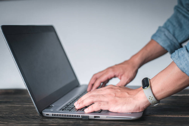 Die Hand eines Mannes, der ein Jeanshemd trägt und eine Geste zeigt, die auf den Computer auf dem Tisch zeigt, Auf weißem Hintergrund, Geschäftskonzept, Technologiekonzept. - Foto, Bild