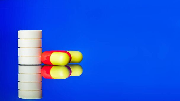 white tablets and red yellow pills on glass with reflection, medical mockup banner isolated on a blue background with copy space, nobody. - Zdjęcie, obraz