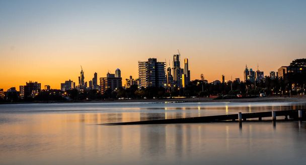 fotografía de larga exposición con reflejos en aguas tranquilas. Los reflejos del horizonte de la ciudad de Melbourne al atardecer en el inmóvil agua del lago Albert Park
 - Foto, Imagen