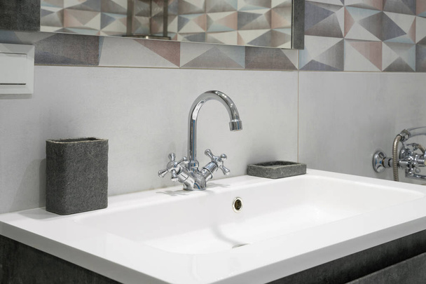 Interior de baño moderno con grifo de metal y fregadero blanco de cerámica. Accesorios de baño y espejo
. - Foto, Imagen