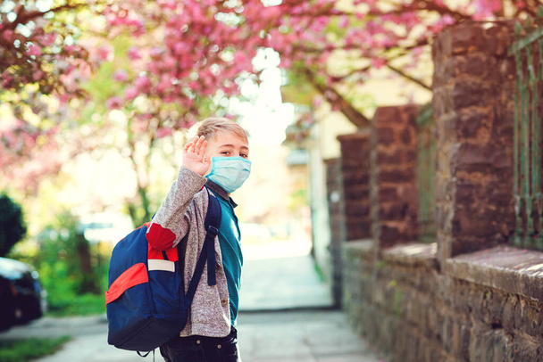 Gelukkige jongen met rugzak die naar school gaat. Schooljongen draagt gezichtsmasker buiten. Onderwijs tijdens de uitbraak van het coronavirus. Terug naar school. Jongen met veiligheidsmasker voor coronaviruspreventie. - Foto, afbeelding