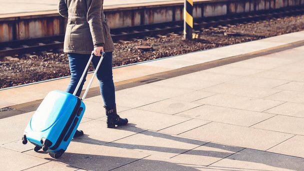 Yurtdışına seyahat etmek için bagaj yolu olan bir kadın yolcu. Tren istasyonunda yürüyen turist kız. Trenle seyahat et. Mavi valiz taşıyan bir kız. Seyahat konsepti. Yaşam tarzı, seyahat, tatil. - Fotoğraf, Görsel