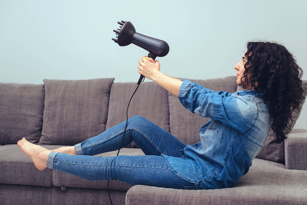 Stylish girl with hairdryer posing at home. Woman makes herself curly hairstyle. Haircare concept. Woman drying hair. Woman styling her curly hair. Girl using hairdryer with special diffuser nozzle. - Photo, image