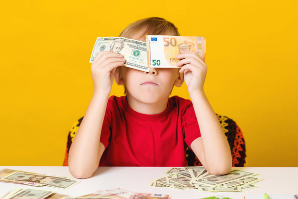 Smart kid covering his eyes with dollar and euro bills. Happy little boy enjoying his income. Saving money for future education. Financial literacy of children. Clever child counting money. - Photo, Image