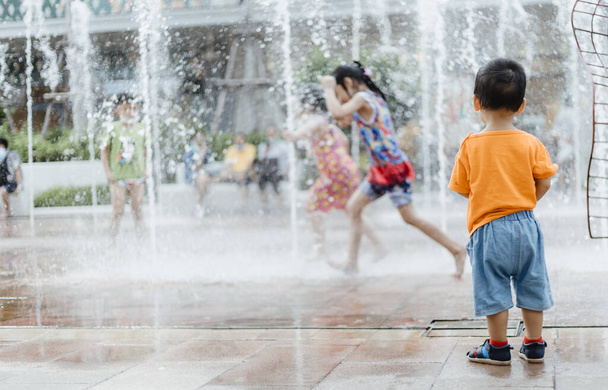 An adorable toddler Asian boy (1-year-old) standing and enjoy to see outdoor public fountains a water splashing for the first time. Thailand plays and fun space for kids. Vacation and holiday concept. - Fotó, kép