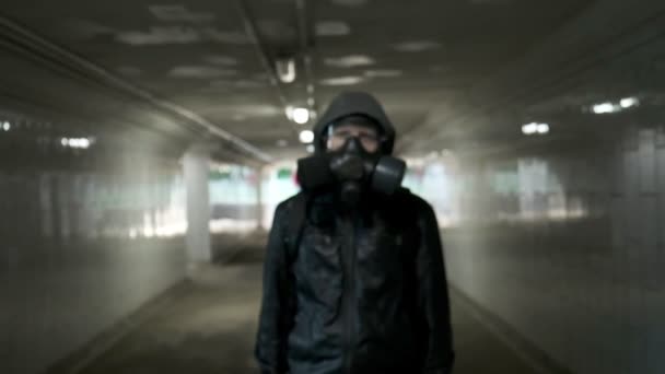 Mann mit Gasmaske, schwarze Jacke mit Kapuze steht in langem Tunnel, Unterführung - Filmmaterial, Video