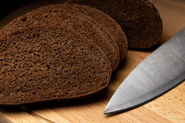 Pan negro en rodajas y un cuchillo en una tabla de madera
 - Foto, Imagen