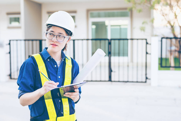 Asian woman engineer or architecture hold clipboard and looking at construction site or work place and checking audit checklist. Concept of engineering design or architecture working audit on site. - Photo, Image