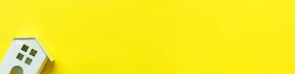 Απλά μίνιμαλ σχεδιασμός με μινιατούρα λευκό παιχνίδι σπίτι απομονωμένο σε κίτρινο πολύχρωμο φόντο. Έννοια κατοικίας για ασφάλιση ενυπόθηκων περιουσιακών στοιχείων. Επίπεδη lay top view αντίγραφο banner χώρο - Φωτογραφία, εικόνα
