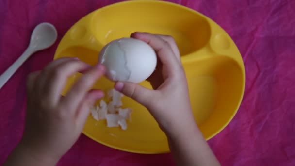 Bovenaanzicht van kinderhanden schil gekookt ei op roze achtergrond met kopieerruimte - Video