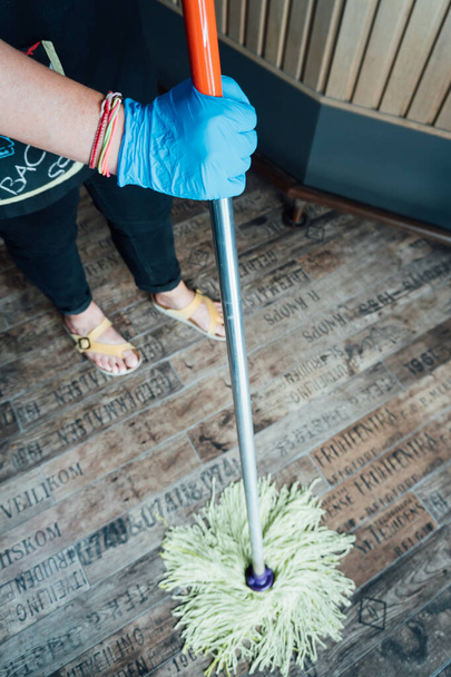Γυναίκα με μπλε γάντια που καθαρίζει το πάτωμα ενός εστιατορίου με μια σφουγγαρίστρα - Φωτογραφία, εικόνα