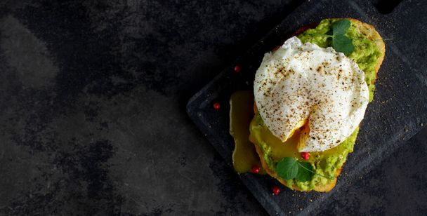 Vista dall'alto dell'uovo in camicia su crema di avocado e pane tostato su sfondo scuro con copyspace - Foto, immagini